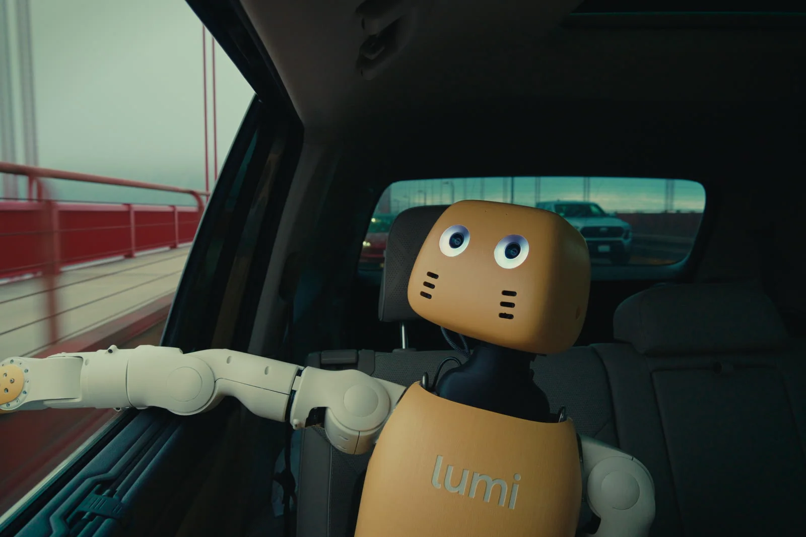A Lumi robot with a rounded yellow head, expressive animated blue-white eyes, and white mechanical arms rests inside the backseat of a car driving across the Golden Gate Bridge.