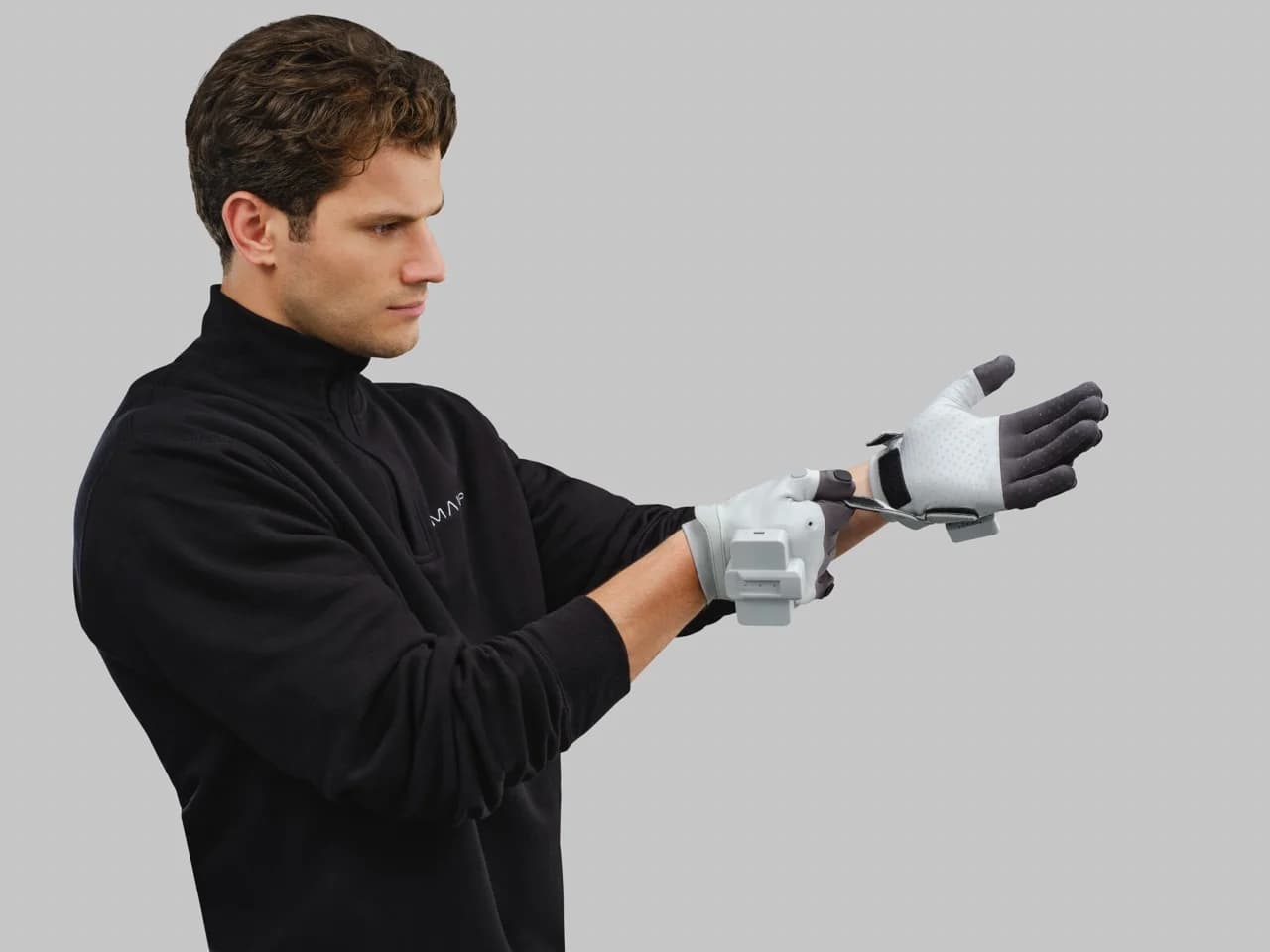 A side profile of a person sliding the detachable Haptic Top Module onto a white and grey haptic sensor glove.