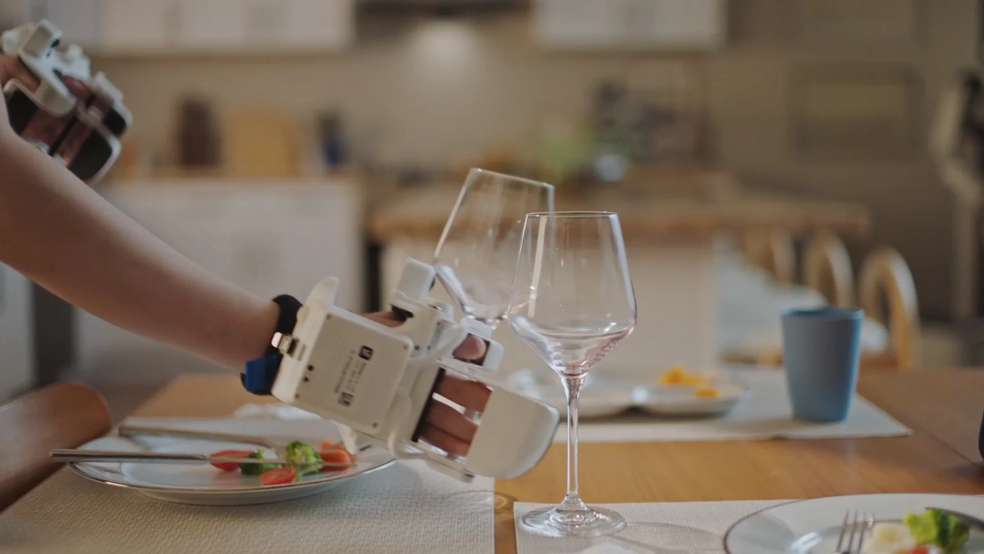 A close-up of a human hand wearing a white, sensor-laden glove, demonstrating a complex maneuver by holding two wine glasses simultaneously by their stems.