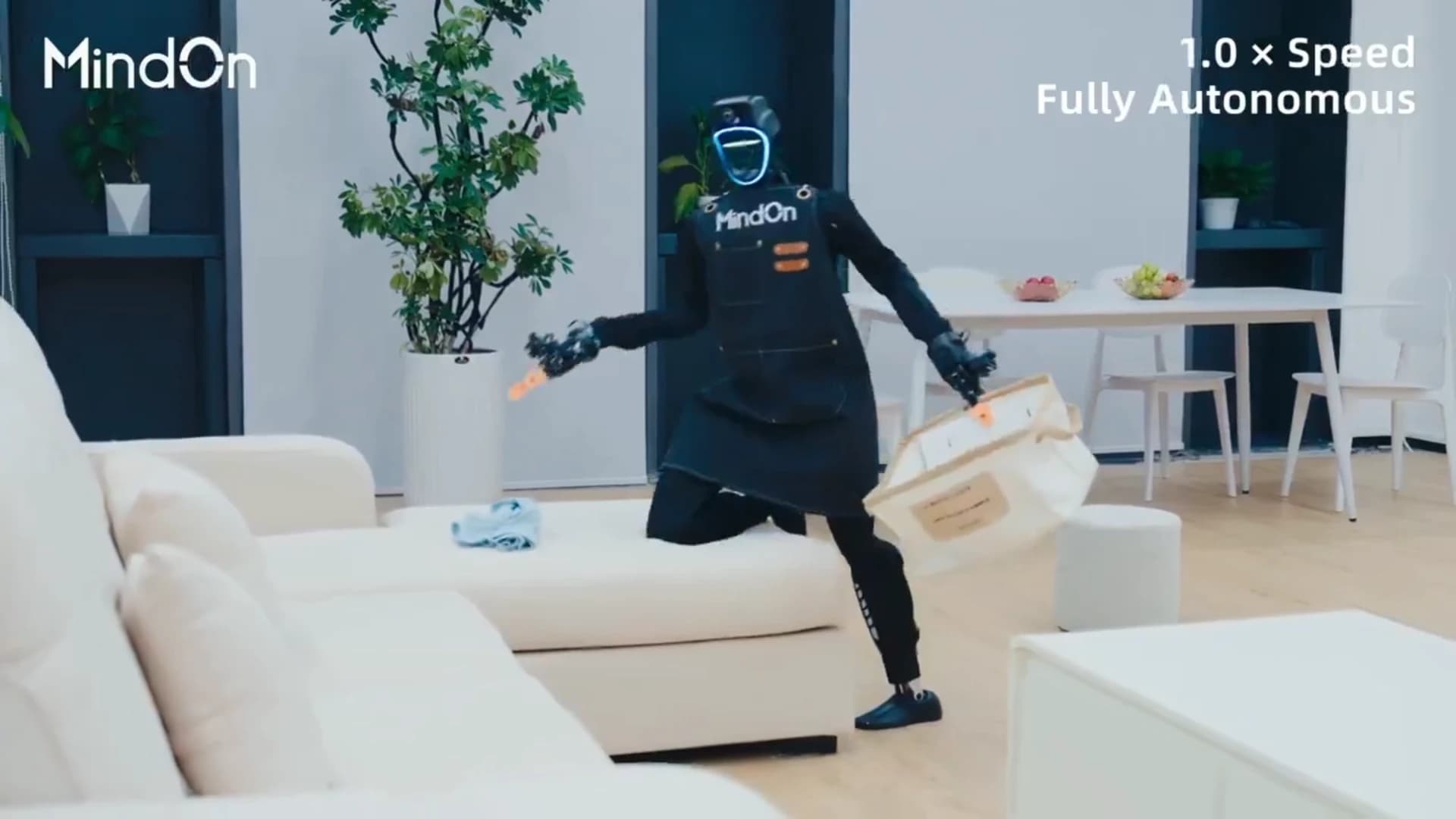 A MindOn-powered humanoid rests one knee on a sofa while holding a laundry basket, with clothing on the cushion and overlays reading 1.0× Speed and Fully Autonomous.