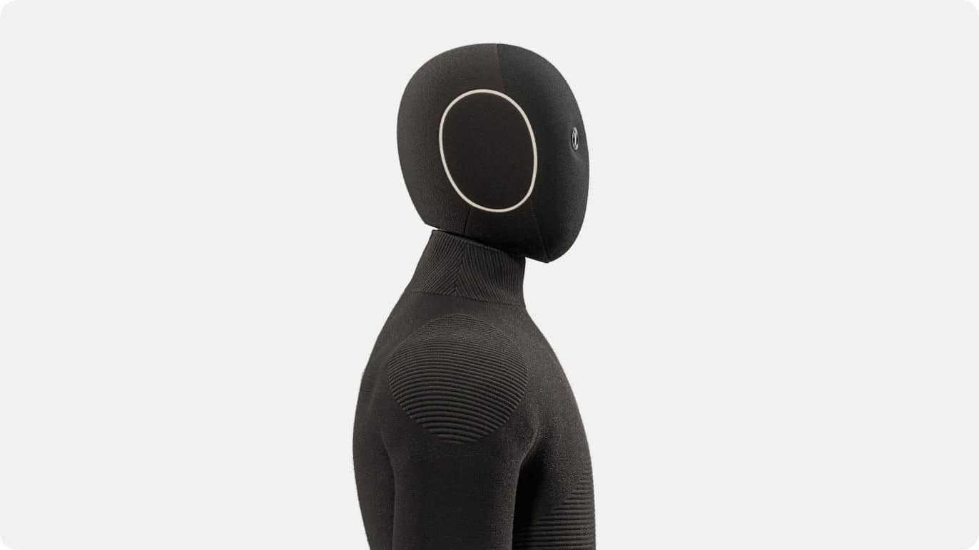 A profile view of the 1X NEO robot, highlighting the soft fabric covering on its head and shoulders and the LED status ring on the side of its head.