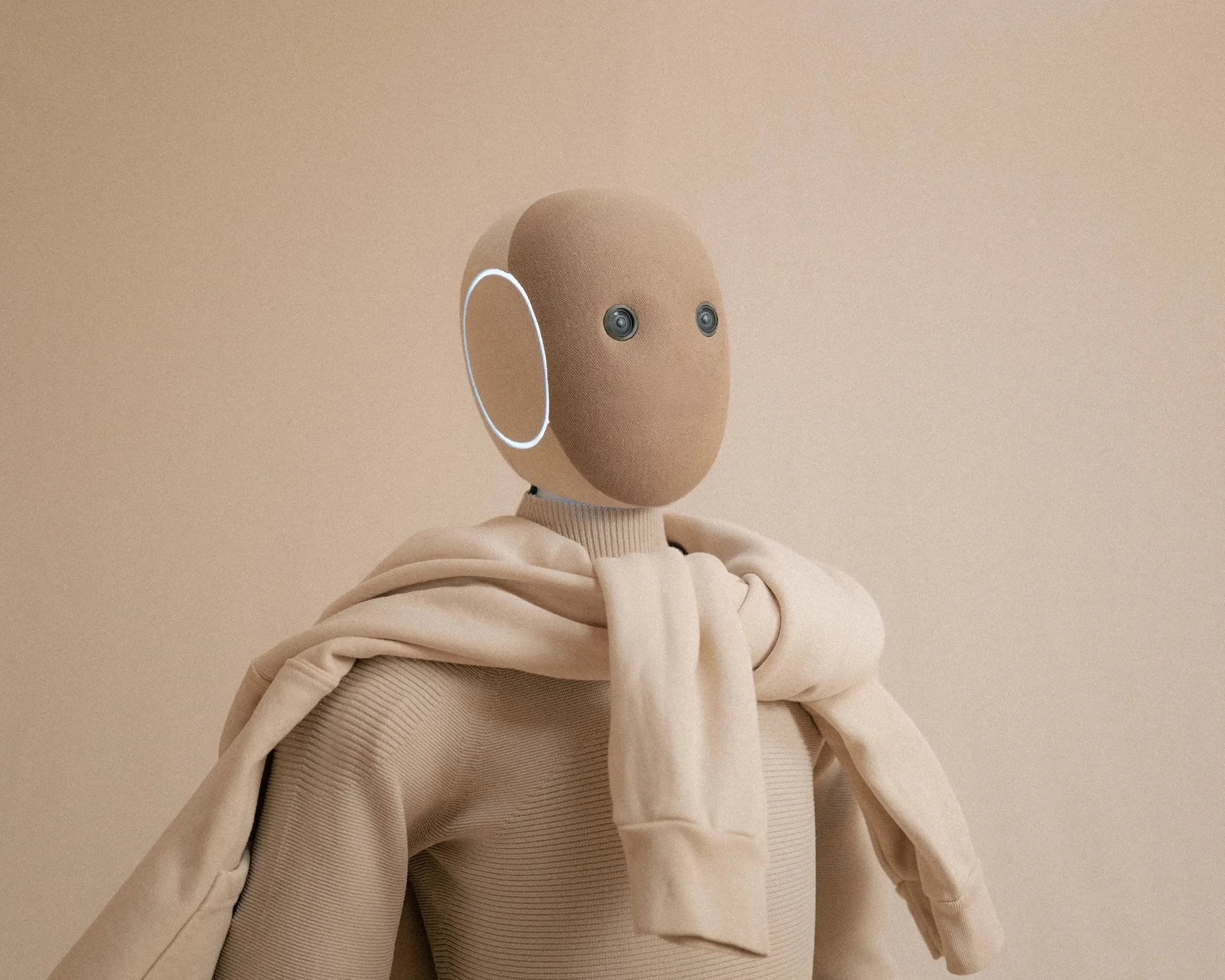 The NEO humanoid robot wearing a beige zip-up hoodie, showing the fabric's soft texture and the robot's camera eyes.