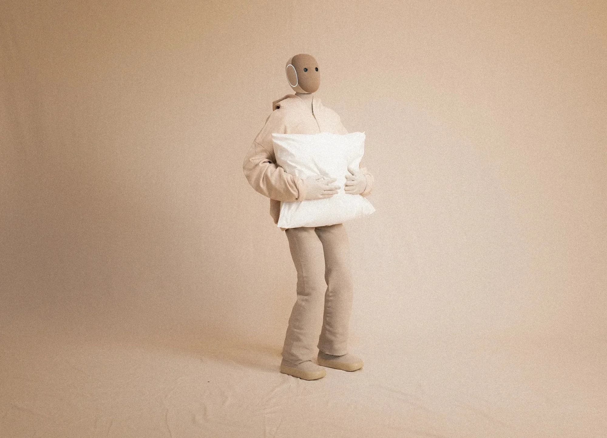 NEO robot standing and holding a large, soft white pillow with both five-fingered hands.