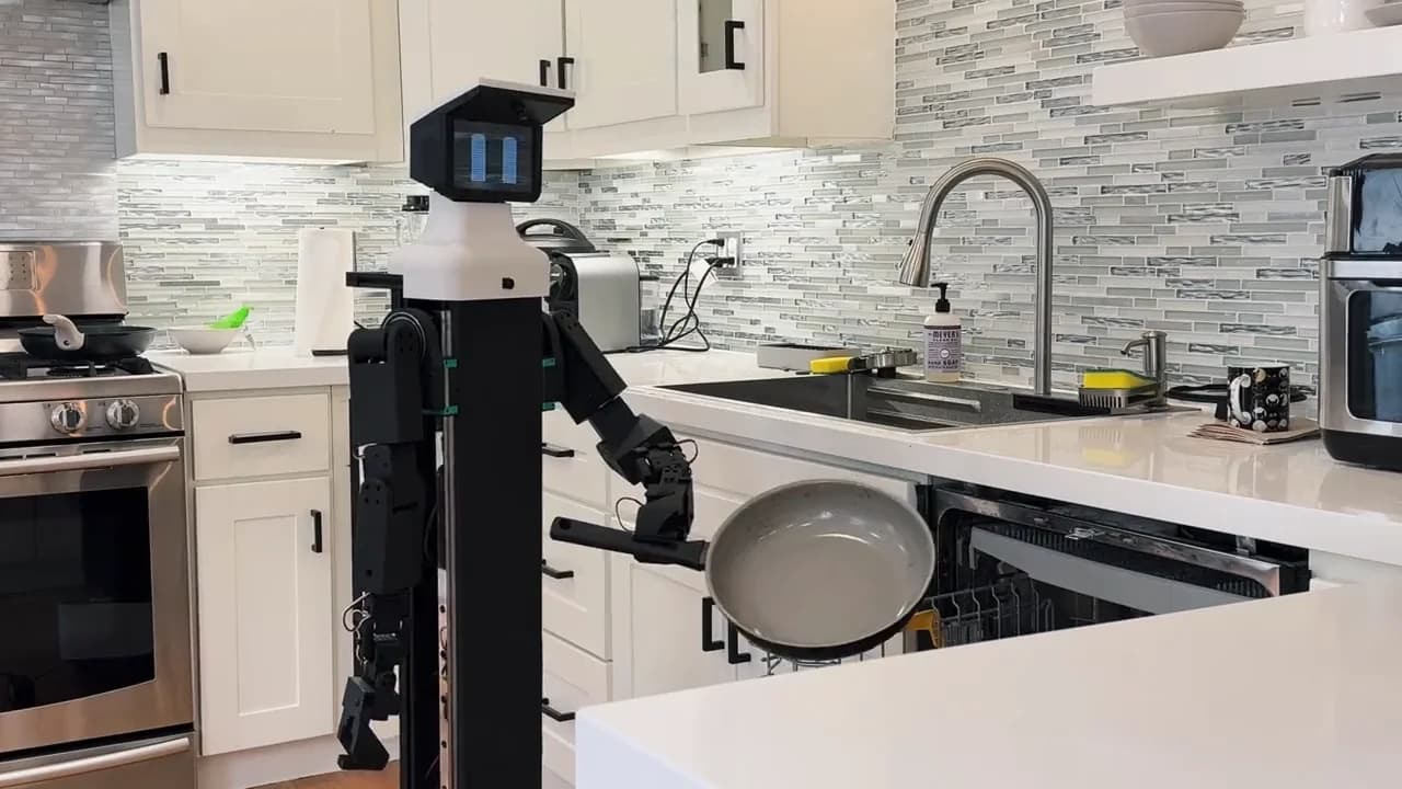 The Nori A3 robot standing in a domestic kitchen setting, featuring a compact wheeled base, a central vertical column, and dual robotic arms with soft grippers.