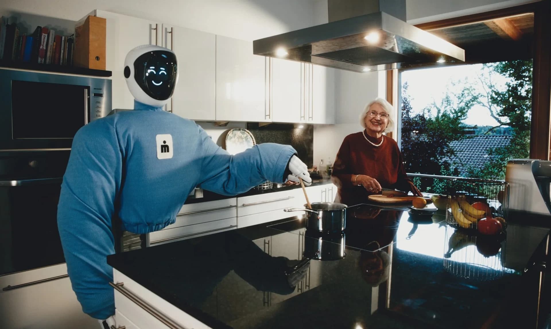 Plim, wearing a blue covering, stirs a pot beside a woman preparing food in a home kitchen.