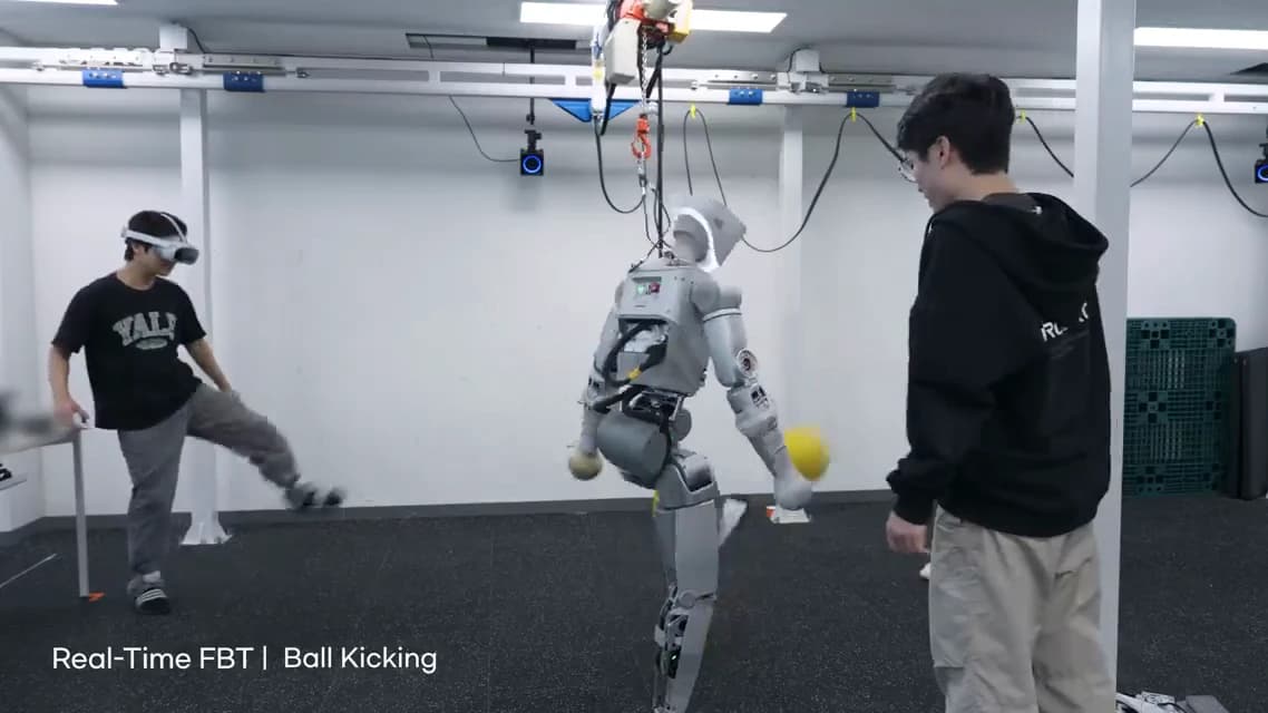 A headset-wearing operator and IGRIS-C lift their legs during a ball-kicking demonstration, with a second person standing beside the robot and overhead safety rigging visible.