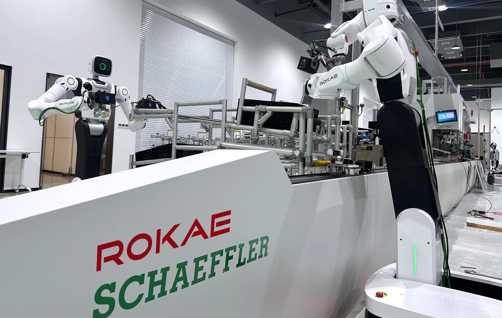ROKAE wheeled humanoid robots beside an assembly line with ROKAE and Schaeffler branding.