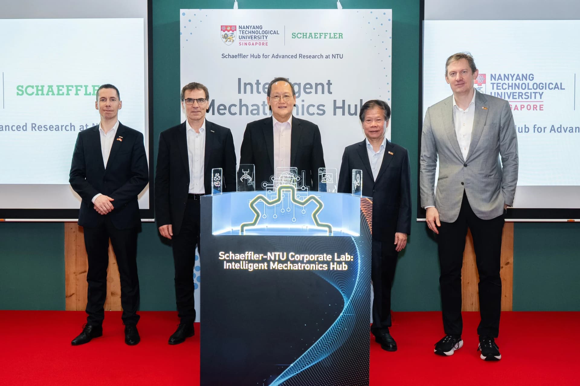Five men stand on a stage behind a futuristic, blue-lit podium reading "Schaeffler-NTU Corporate Lab." A presentation screen behind them displays the logos of Nanyang Technological University and Schaeffler.