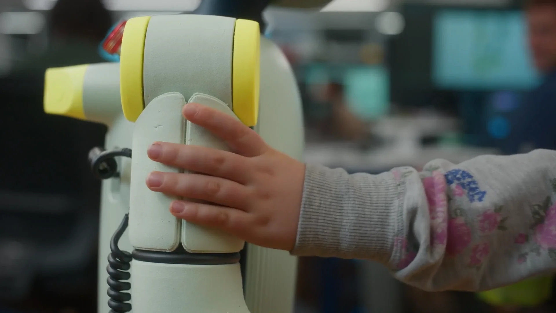 A close-up of a child's hand pressing into the soft, light-green foam material of one of the Sprout robot's limbs.