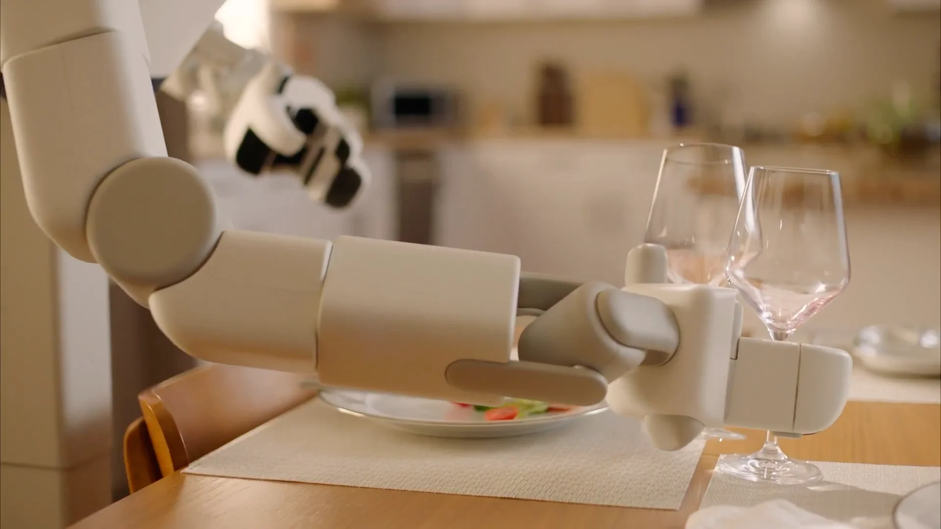 A close-up of the Sunday Robotics end-effector, showing a custom dual-gripper with two separate pincers, simultaneously picking up two empty wine glasses from a table.