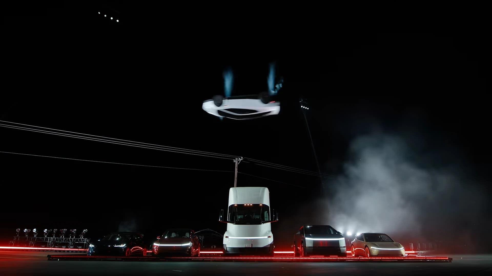 A Tesla Roadster upside down in midair above a lineup of Tesla vehicles during the kickflip demonstration.