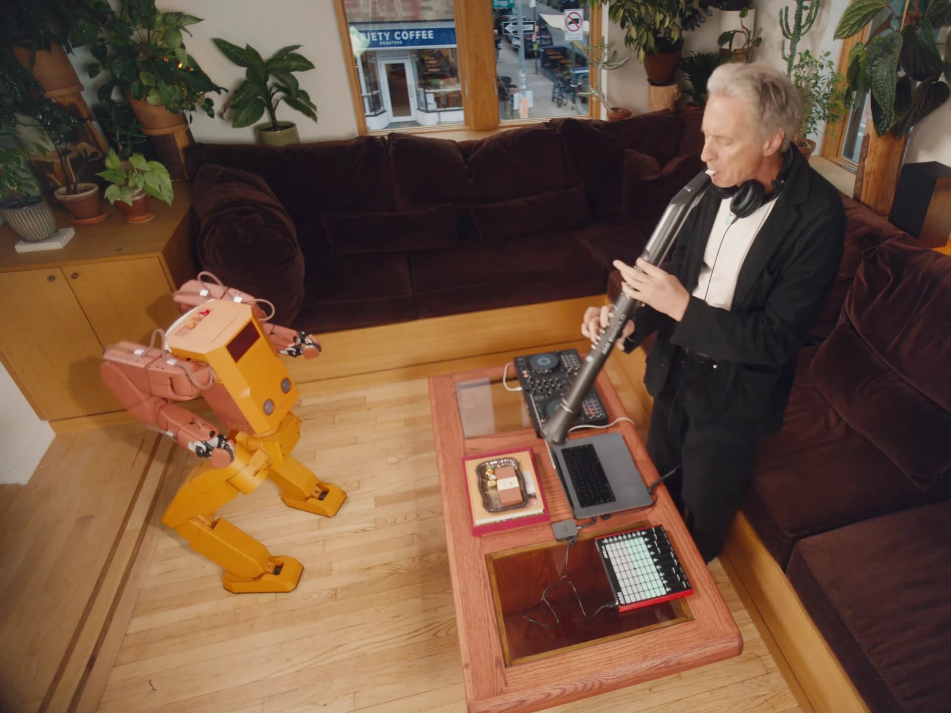 Voxel beside a musician playing a wind instrument in a plant-filled living room.