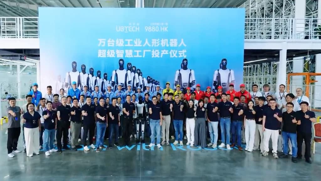 UBTECH executives, engineers, and government officials give a thumbs-up in front of a blue backdrop celebrating the commissioning of the 10,000-unit industrial humanoid factory, with a Walker S series robot standing at the center.