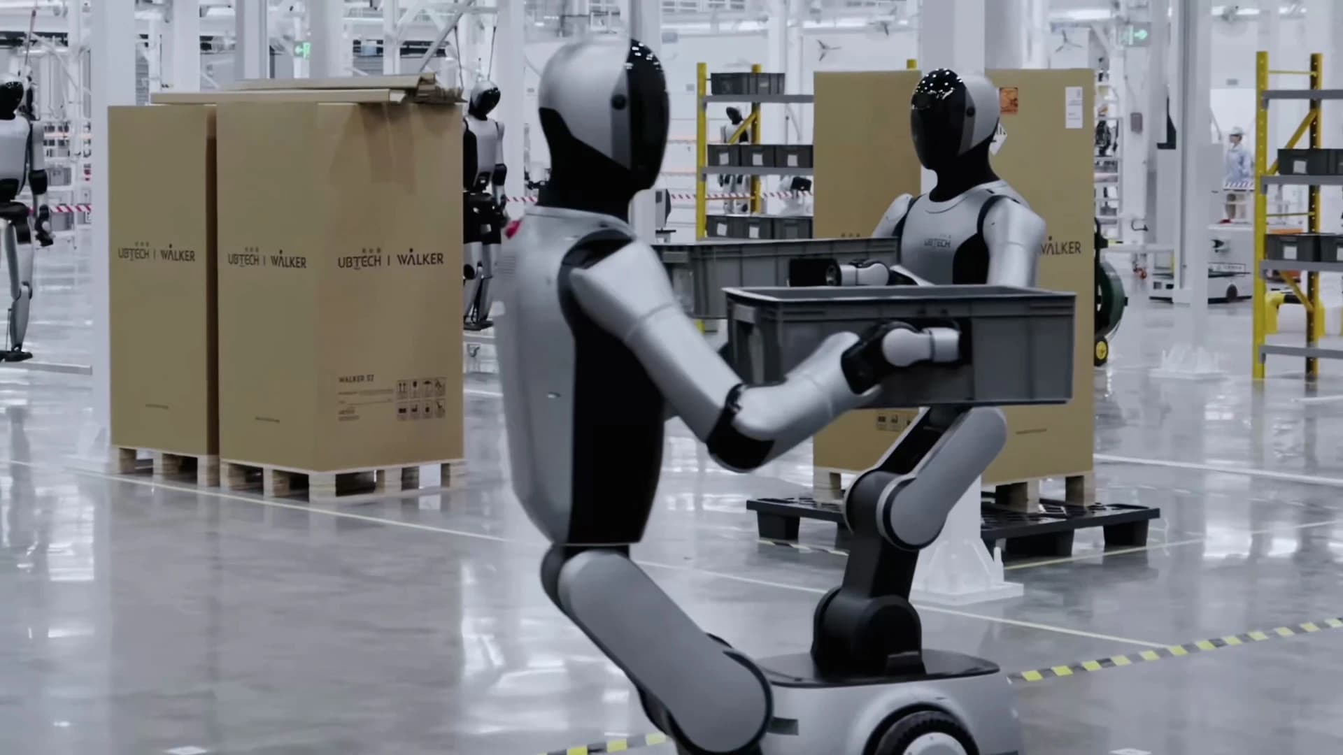 UBTECH robots carrying gray containers inside the company’s factory, alongside boxed Walker robots.