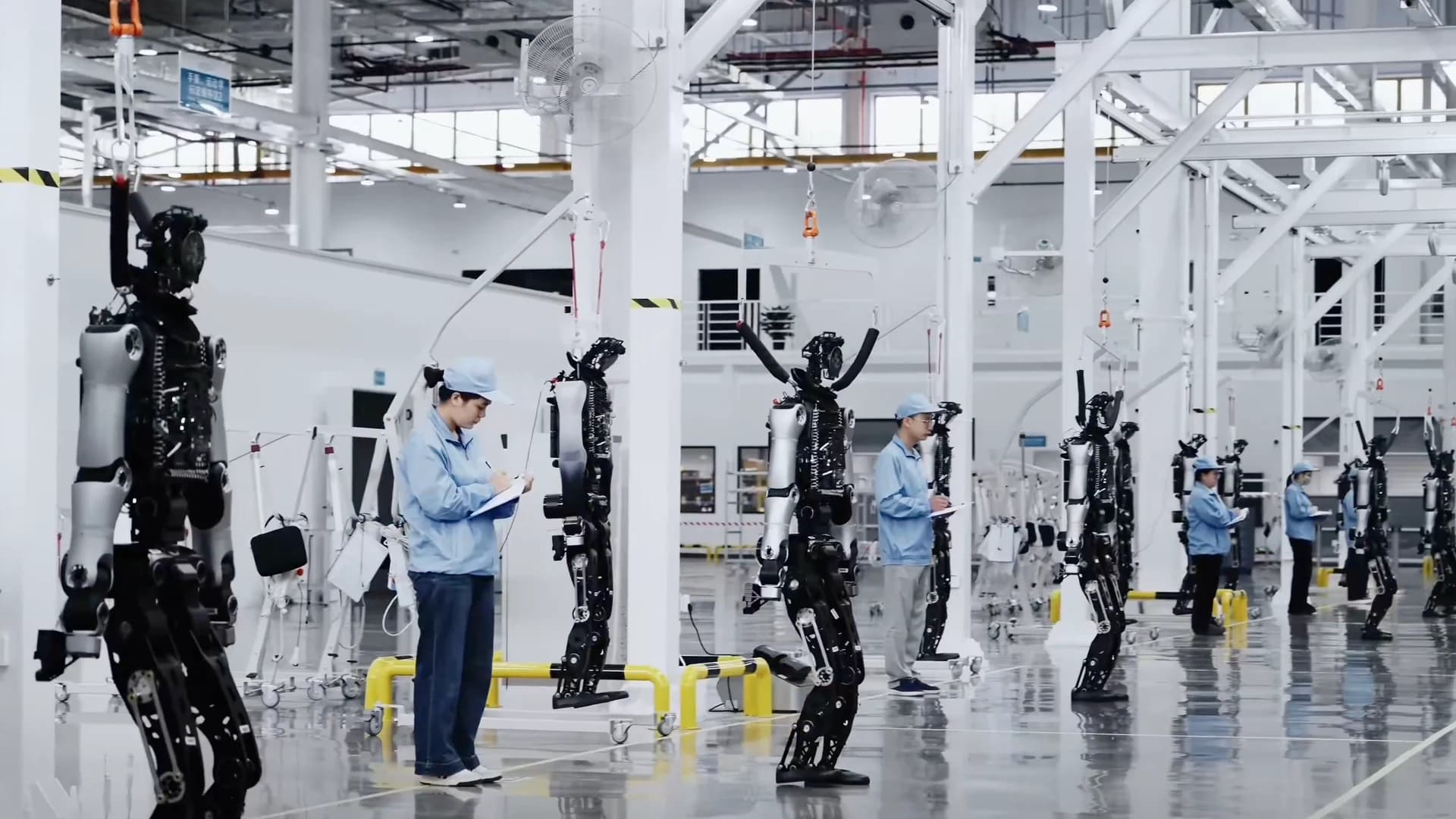 Workers stand alongside a row of humanoid robots on the UBTECH factory floor.