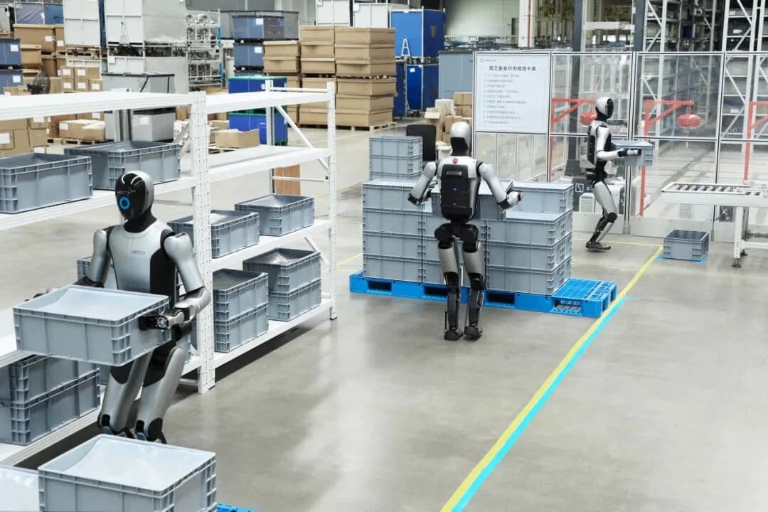 Three UBTECH humanoid robots handling grey containers beside factory shelving and a conveyor.