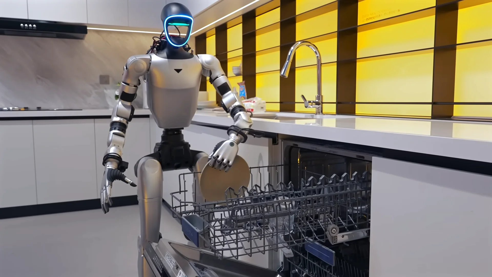 A silver and black Unitree humanoid robot standing in a modern kitchen with yellow backlighting. The robot features a glowing blue visor and is using its articulated hand to carefully place a tan plate into the bottom rack of an open dishwasher, as seen in image_45732f.png.