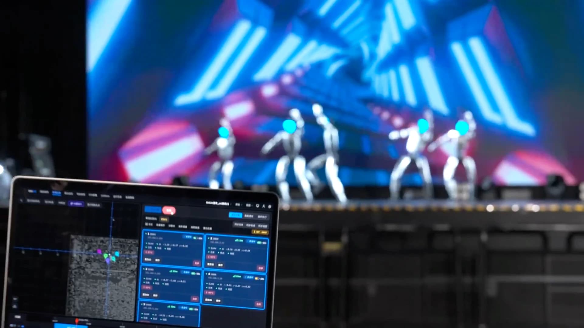 A laptop displays UniUni robot monitoring software while humanoid robots perform on a stage behind it.