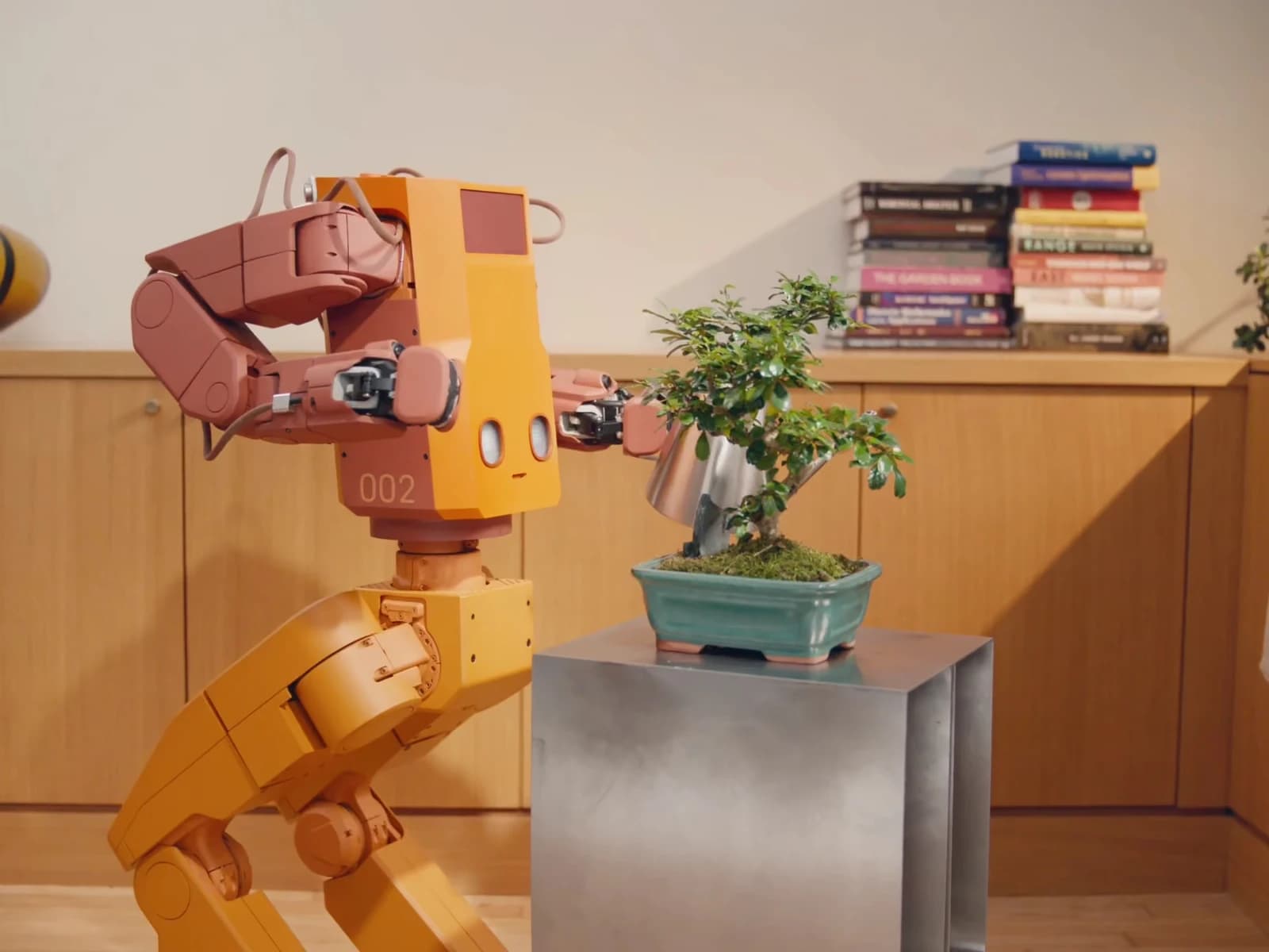 Tuesday Labs’ yellow Voxel robot holding a watering can beside a bonsai tree.
