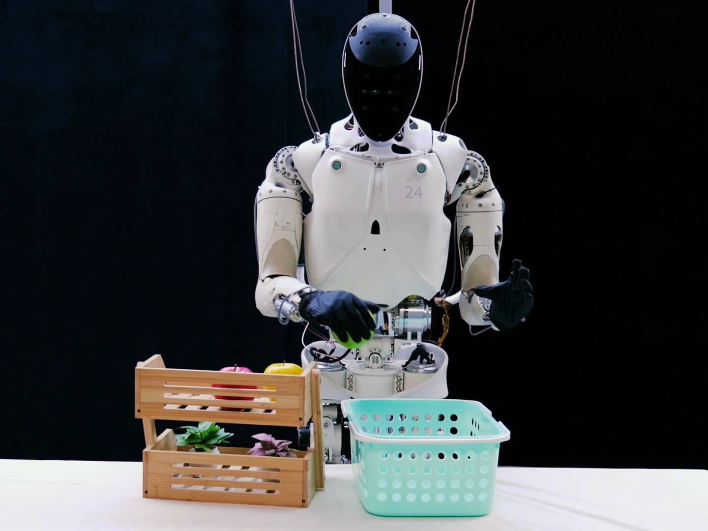 Previous-generation XPENG IRON holding a green apple above a table beside a basket during an XPACE demonstration.